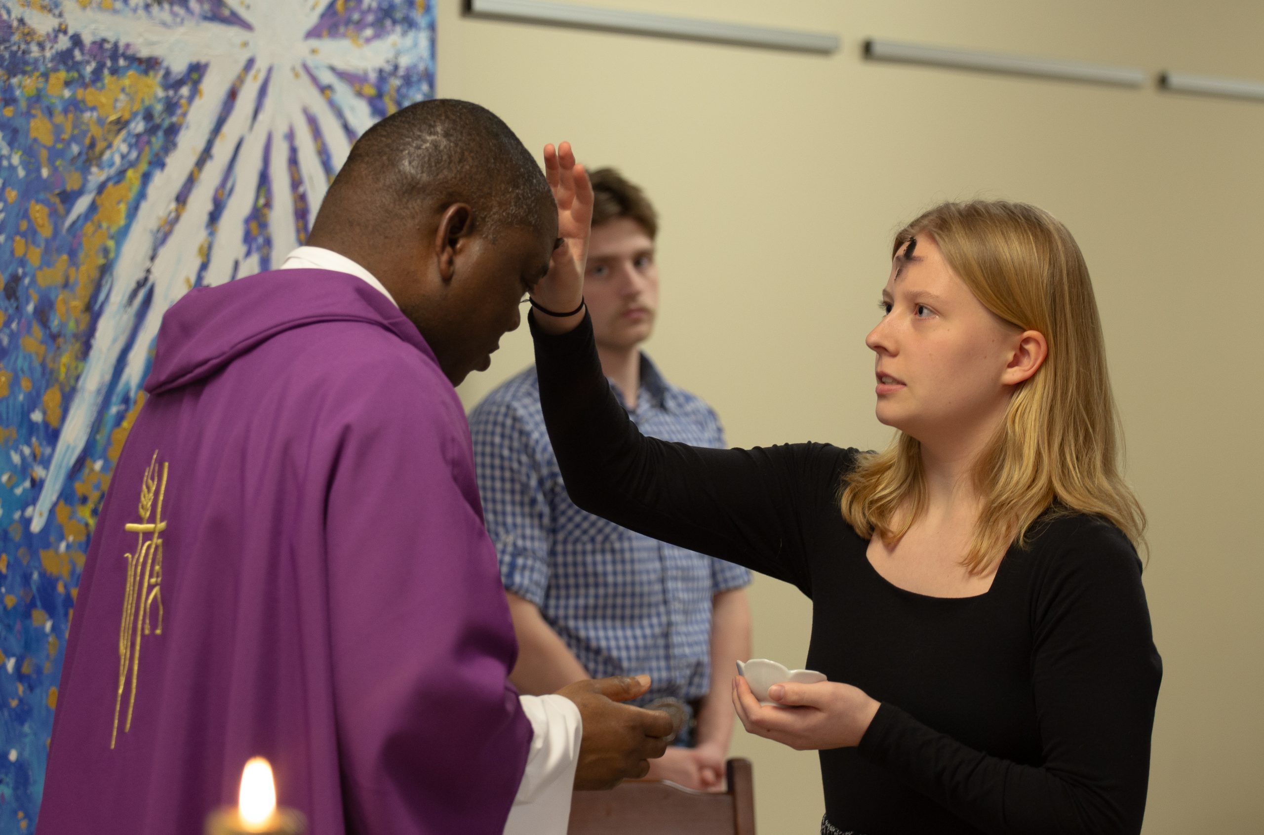 A female student marks a priest's forehead with ashes at Mass on Ash Wednesday. This is an example of courageous ministry.